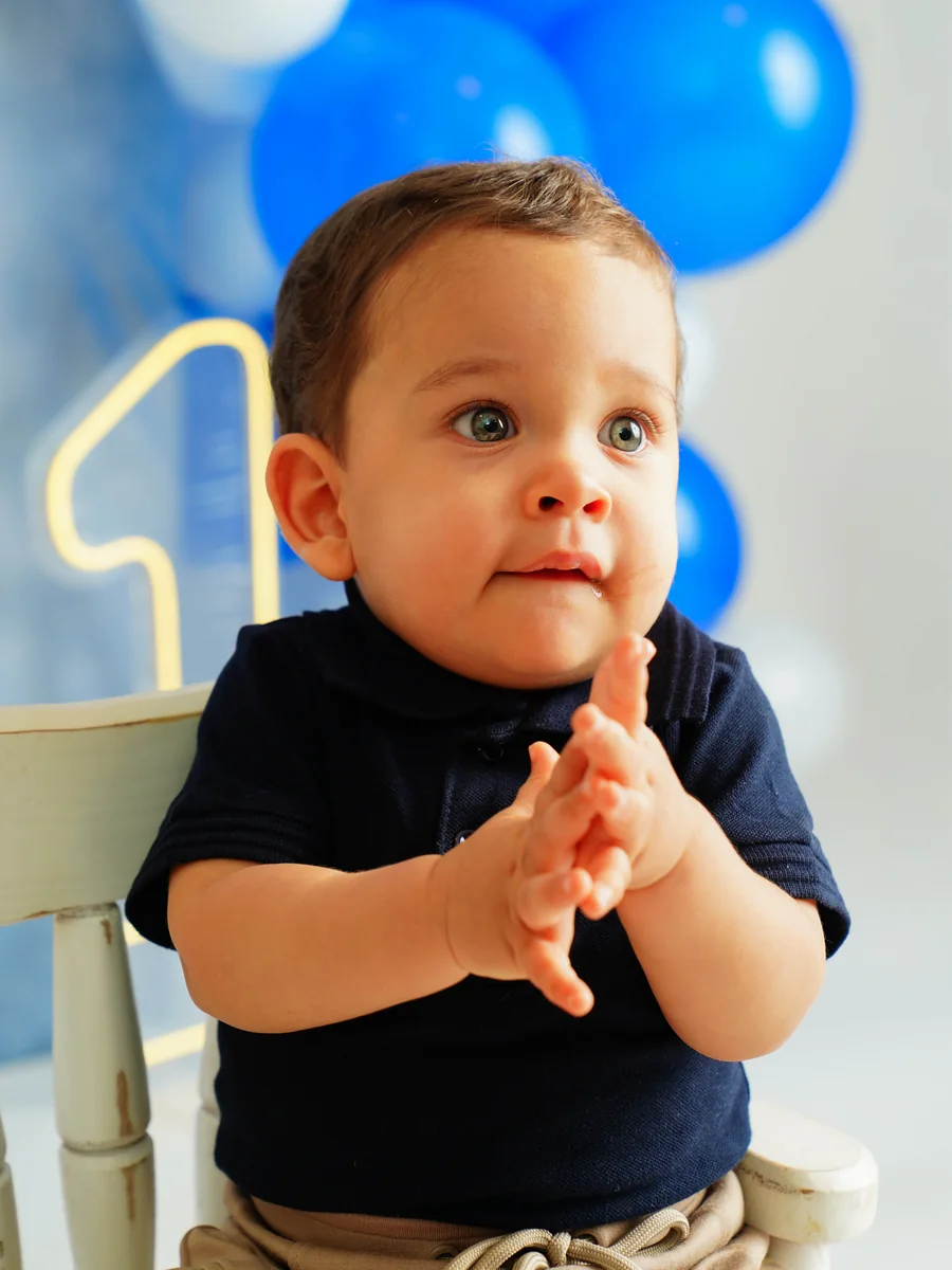Bebê batendo palmas diante de balões azuis e do número 1 — ensaio infantil de 1 aninho em Brasília