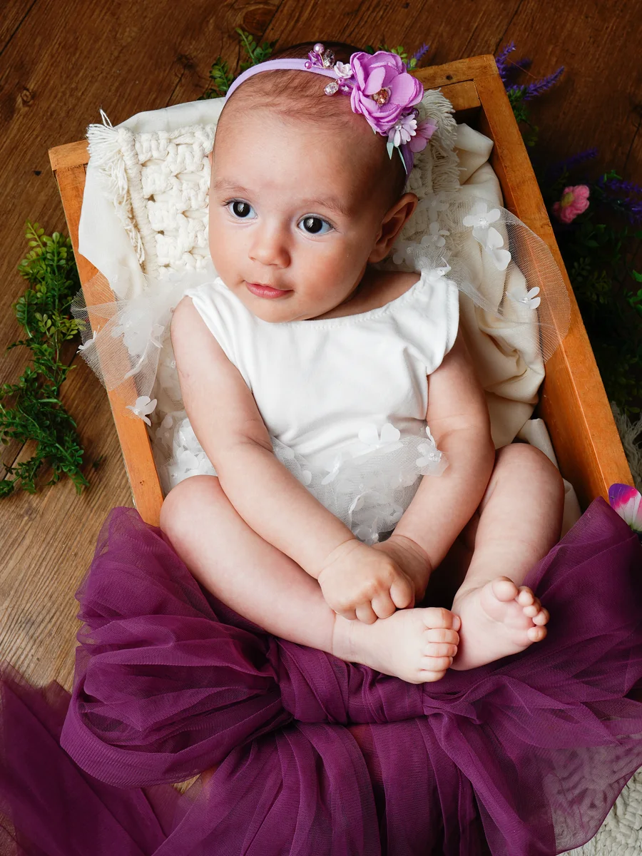 Bebê de tiara de flores sentada sobre tule bordô, num cesto de madeira — ensaio infantil de 3 meses em Brasília