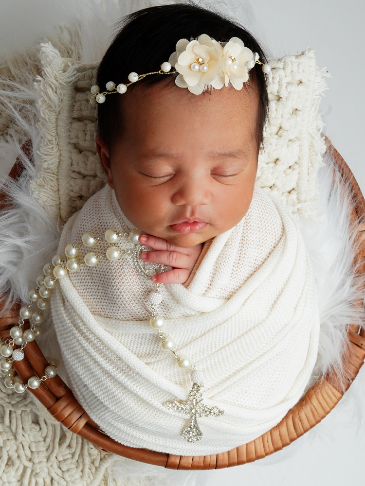 Newborn dormindo num cesto de vime com terço de pérolas e cruz — ensaio newborn temático em Brasília